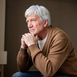 Man sitting with chin resting on hands and staring into space